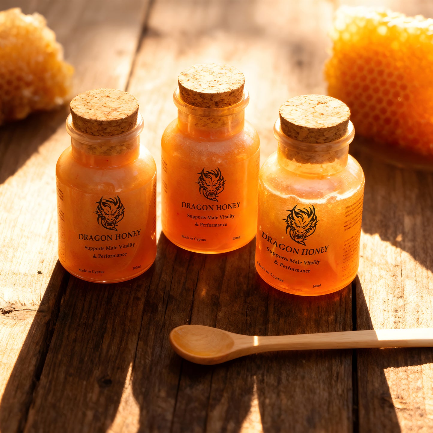 Three jars of Dragon Honey on a wooden surface with a honeycomb and a spoon.